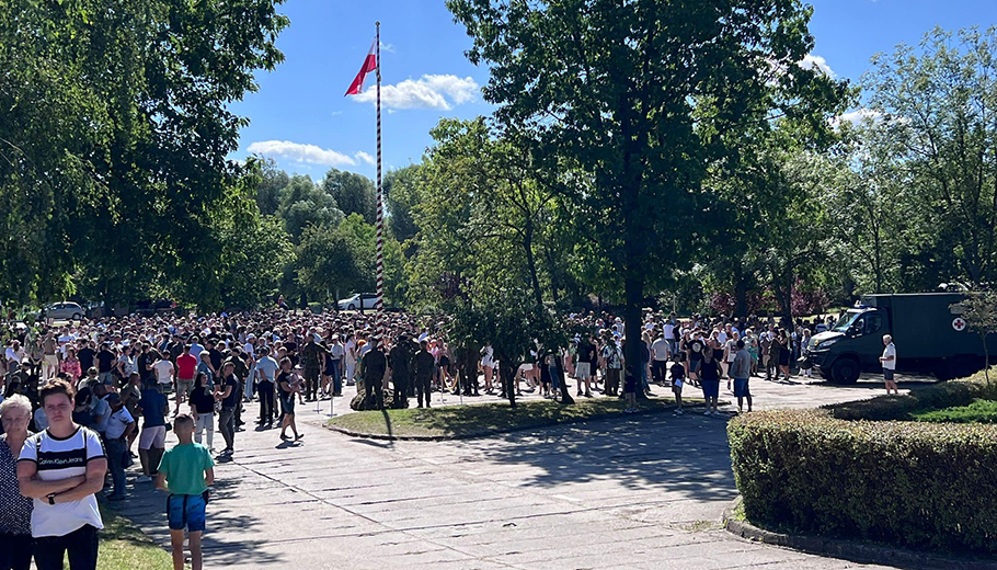 tłum ludzi - gości i widzów na płycie parkingu. pośrodku masz z flagą państwową 